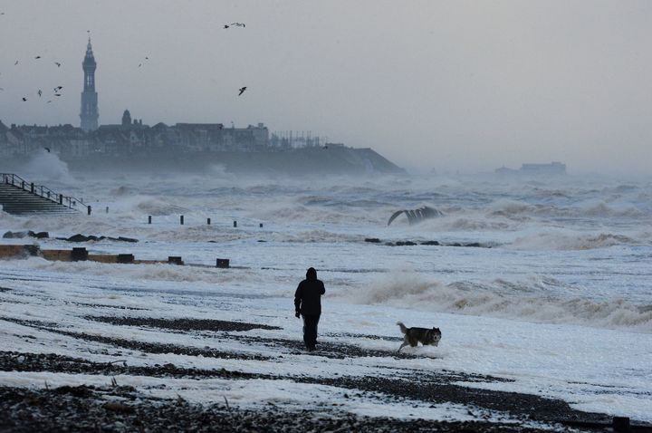 A man walks his dog along windy beach at Cleveleys near Blackpool as high winds have brought another day of disruption to Britain's transport networks as warnings remain in place for fierce gusts, snow and ice over much of the weekend.