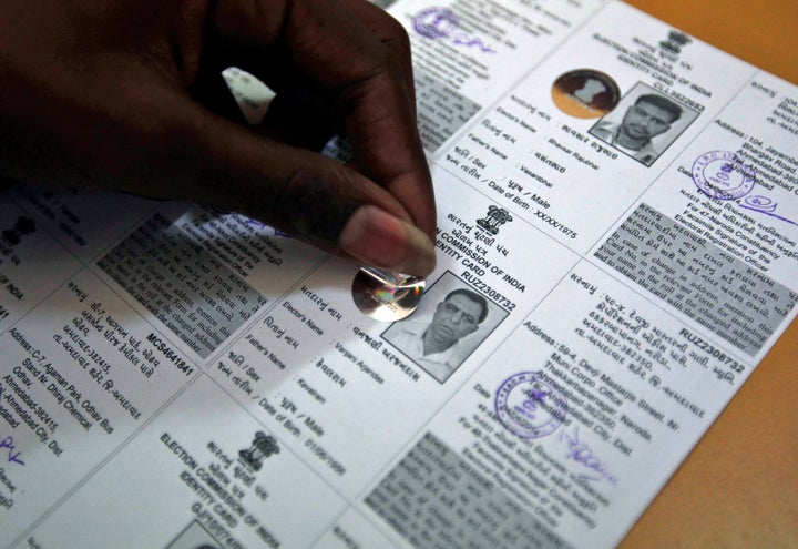 An election staff member pastes a hologram on a voter identification card.