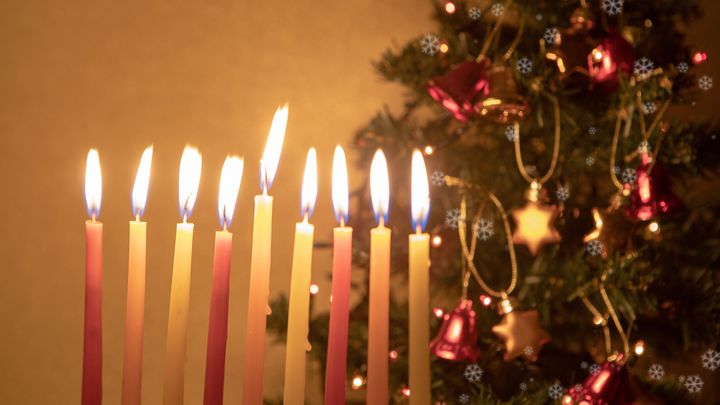 Hanukkah candles burn on the background of a Christmas tree