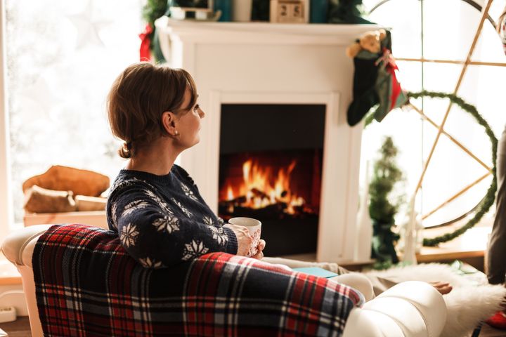 Woman sitting on sofa, holding cup of coffee by the fireplace at Christmas day