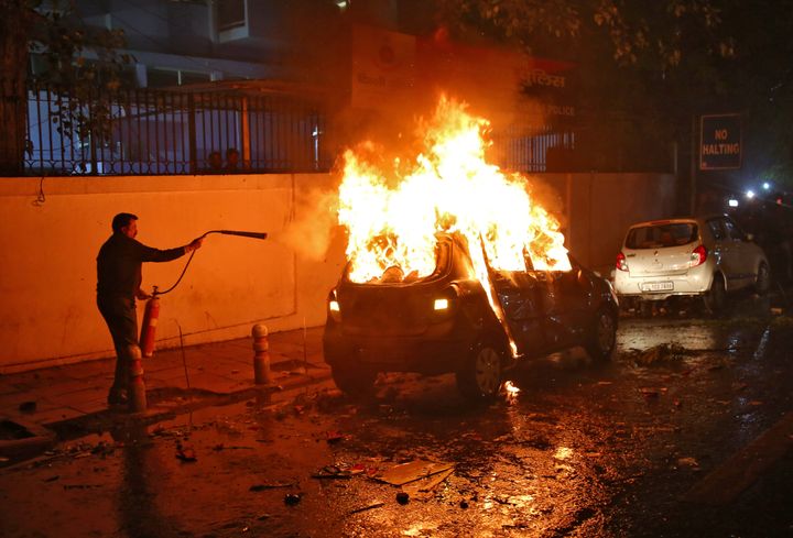 A man tries to extinguish a burning car after demonstrators set it on fire during a protest against a new citizenship law, in New Delhi, India