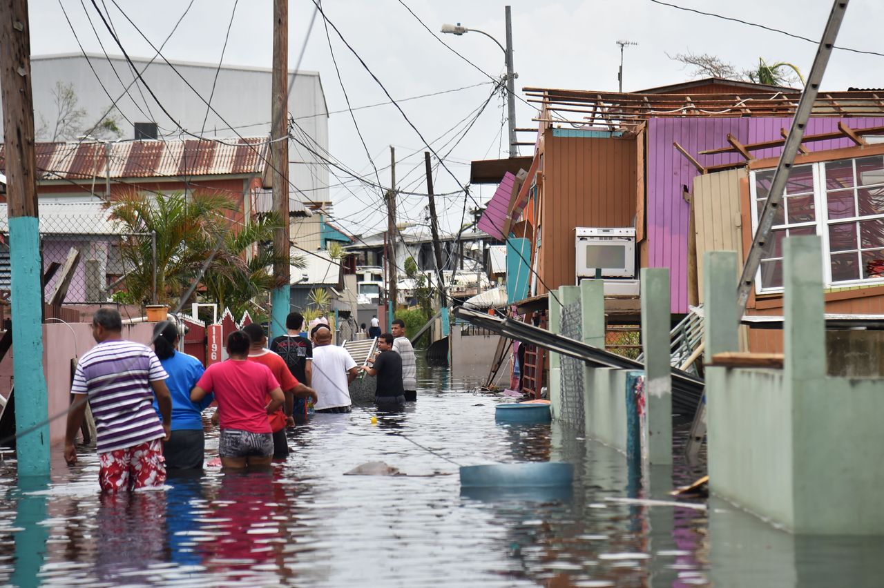 People walk in a flooded street next to damaged houses in Puerto Rico on September 21, 2017, after Hurricane Maria hit.