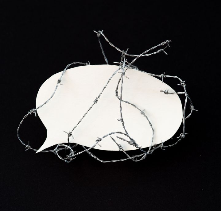 Barbed wire around a speech bubble made of paper. Black background.