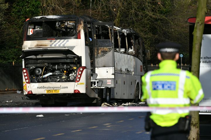 A police officer looks on at the burnt remains of a coach in Queenstown Road, south west London, after one person died and three others were injured in a collision between the coach and a car.