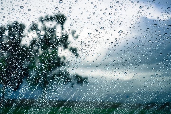 Drops of rain on the window; blurred trees and storm clouds in the background;