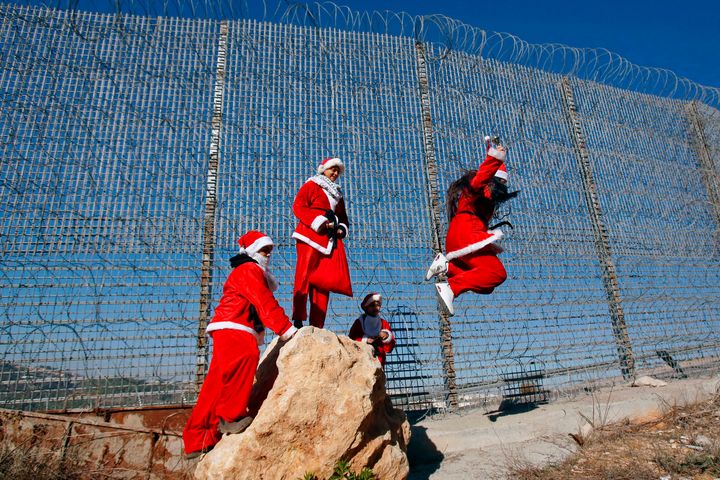 Παλαιστίνιοι φορώντας στολές Άγιου Βασίλη χοροπηδούν πλάι στον συρματένιο φράχτη που έχουν υψώσει οι Ισραηλινοί κοντά στο χωριό Γουλατζέχ, δυτικά της Βηθλεέμ