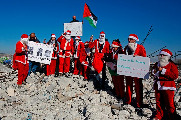 Με στολές Άγιου Βασίλη, Παλαιστίνιοι διαμαρτύρονται κατά της ισραηλινής κατοχής στα ερείπια ενός σπιτιού που οι αρχές του Ισραήλ κατεδάφισαν επειδή, όπως υποστηρίζουν, δεν έχει λάβει νόμιμη άδεια. Χωριό αλ Καντέρ, δυτικά τής Βηθλεέμ
