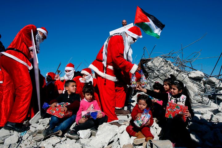 Η σημαία της Παλαιστίνης στα ερείπια σπιτιού που κατεδάφισαν οι ισαρηλινές αρχές. Παιδιά και άνδρες ντυμένοι με στολές Άγιου Βασίλη και μοιράζουν δώρα. Χωριό αλ Καντέρ, δυτικά της Βηθλεέμ. 