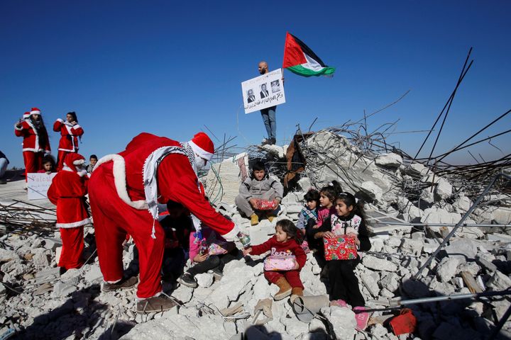 Η σημαία της Παλαιστίνης στα ερείπια σπιτιού που κατεδάφισαν οι ισαρηλινές αρχές. Άνδρες ντυμένοι με στολές Άγιου Βασίλη μοιράζουν δώρα σε παιδιά Χωριό αλ Καντέρ, δυτικά της Βηθλεέμ.
