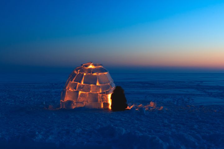 At dusk, the snow house is lit by candles from the inside.