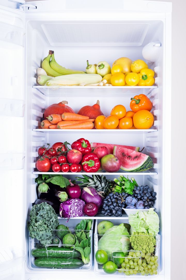 Opened refrigerator full of vegetarian healthy food, vibrant colour vegetables and fruits inside on fridge