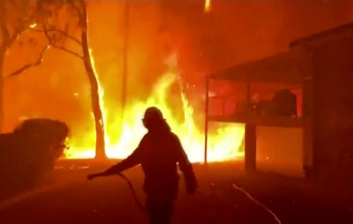 In this image made from video taken and provided by NSW Rural Fire Service via their twitter account, a firefighter sprays water on a fire moving closer to a home in Blackheath, New South Wales state, Australia Sunday, Dec. 22, 2019. Prime Minister Scott Morrison on Sunday apologized for taking a family vacation in Hawaii as deadly bushfires raged across several states, destroying homes and claiming the lives of two volunteer firefighters.(Twitter@NSWRFS via AP)