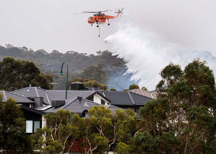 A skycrane drops water on a bushfire in scrub behind houses in Bundoora, Melbourne.
