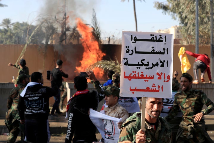 A Hashd al-Shaabi fighter holds a sign reading "Close the American embassy otherwise people will close it" as others set fire