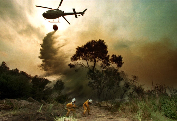 Two firemen fight a bushfire as a helicopter drops water on the blaze in the southern Sydney suburb of Menai on Dec. 3, 2019.