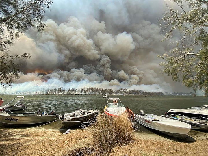 Boats are pulled ashore as smoke and wildfires rage behind Lake Conjola, Australia, on Thursday.