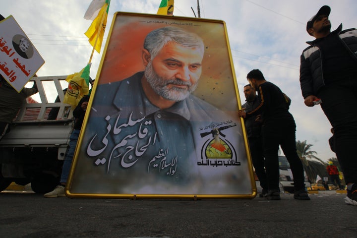 Mourners stand next to a giant portrait for Qassem Soleimani during a funeral procession.