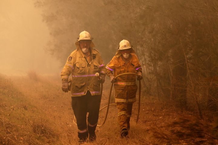 Firefighters drag their water hose after putting out a spot fire near Moruya, Australia, Saturday, Jan. 4, 2020.