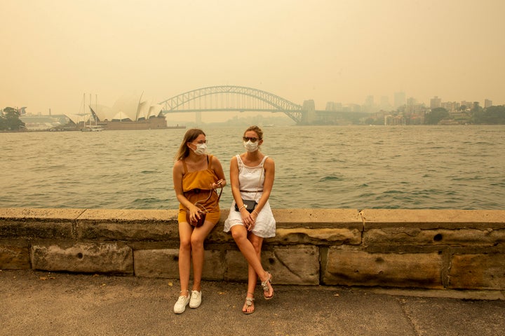 German tourists Julia Wasmiller (left) and Jessica Pryor look on at Mrs Macquarie's chair, wearing face masks due to heavy smoke on Dec. 19 in Sydney.