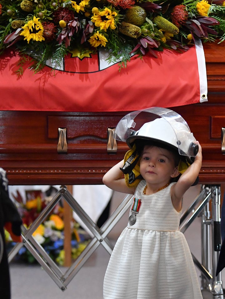 Charlotte O'Dwyer, the young daughter of Rural Fire Service volunteer Andrew O'Dwyer, stands in front of her father's casket wearing his helmet after being presented with his service medal during his funeral on Tuesday. O'Dwyer was one of three firefighters killed in recent fires.