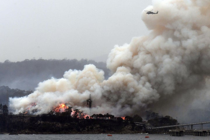 TOPSHOT - A military helicopter flies above a burning woodchip mill in Eden, in Australia's New South Wales state on January 6, 2020. - January 5 brought milder conditions, including some rainfall in New South Wales and neighbouring Victoria state, but some communities were still under threat from out-of-control blazes, particularly in and around the town of Eden in New South Wales near the Victorian border. (Photo by SAEED KHAN / AFP) (Photo by SAEED KHAN/AFP via Getty Images)