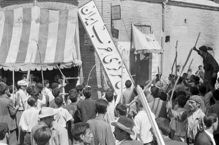 FILE -- In this August 19, 1953 file photo, a crowd of demonstrators tears down the Iran Party's sign from the front of the headquarters in Tehran, Iran, during the pre-Shah riot which swept through the capital and ousted Persian Prime Minister Dr. Mossadegh and his government. On Tuesday, Aug. 27, 2013, Iran's parliament approved fast tracking debate on a bill that seeks to sue the U.S. for its involvement in the 1953 coup that overthrew the country’s democratically elected prime minister. Newly declassified documents revealed recently offer more details of how the CIA orchestrated the overthrow of Iranian Prime Minister Mohammed Mossadegh 60 years ago. (AP Photo, File)