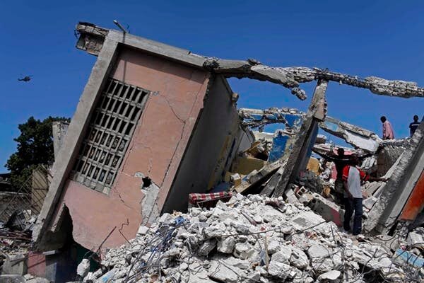 Des personnes se tiennent dans les décombres d’un bâtiment effondré à la suite du séisme, à Port-au-Prince.