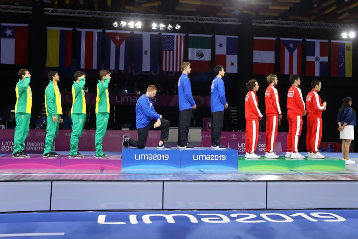 Fencing gold medalist Race Imboden of the United States takes a knee during the national anthem at the Pan American Games on 