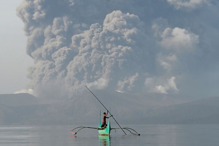 A child living at the foot of Taal volcano rides a canoe while the volcano spews ash 