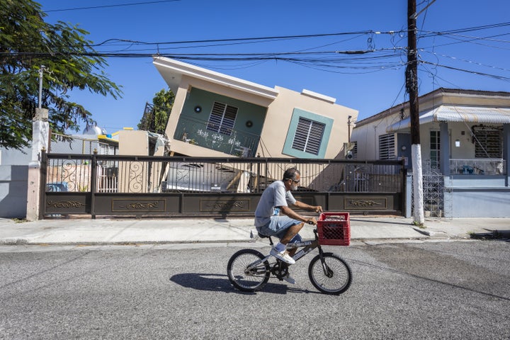A man rides his bike in front of a collapsed house after a 6.4-magnitude earthquake hit Guanica, Puerto Rico, on Jan. 11, 202