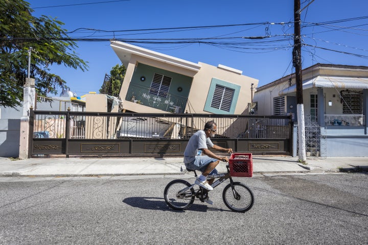 A man rides his bike in front of a collapsed house after a 6.4-magnitude earthquake hit Guanica, Puerto Rico, on Jan. 11, 2020.