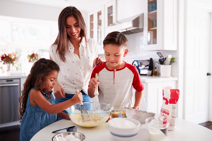 Brother and sister making cake mixture together at the kitchen table with their mum, waist up