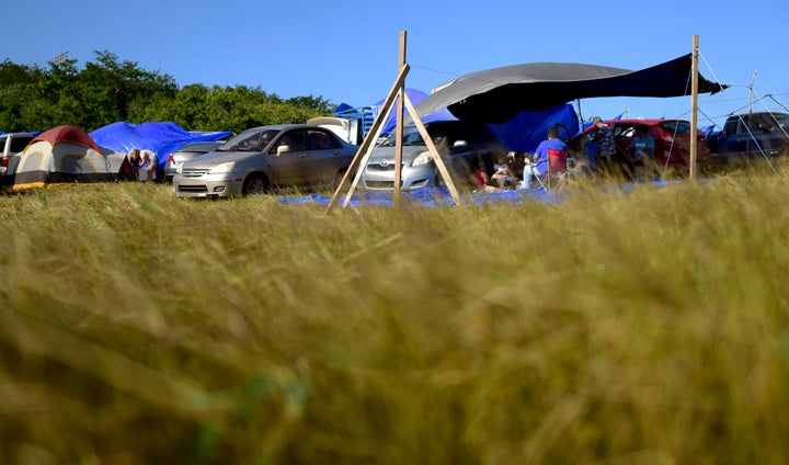 In this Friday, Jan. 10 photo, people shade themselves under a tarp on a private hay farm where residents from the Indios neighborhood affected by earthquakes set up shelter amid aftershocks in Guayanilla, Puerto Rico. 