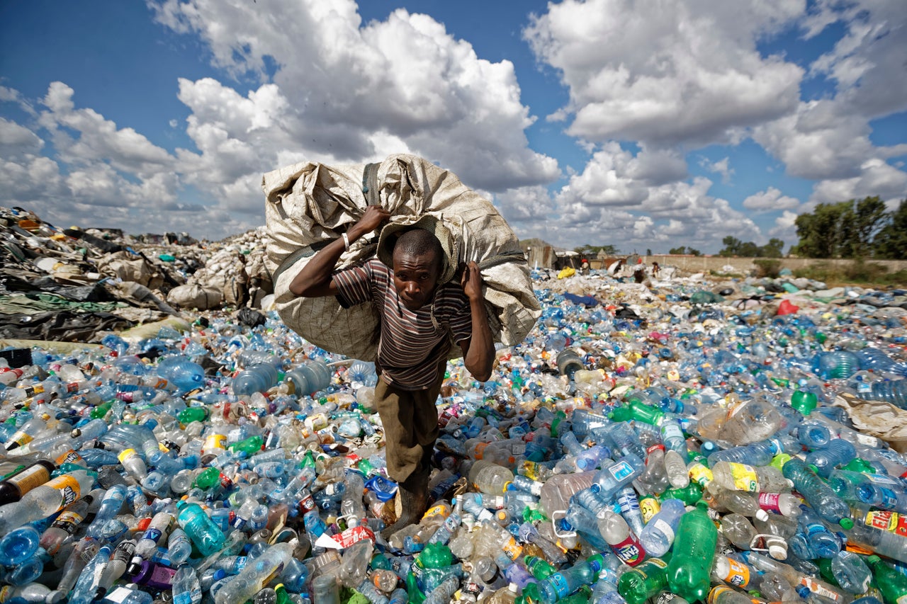 A man walks on a mountain of plastic bottles as he carries a sack of them to be sold for recycling after weighing them at the dump in the Dandora slum of Nairobi, Kenya.