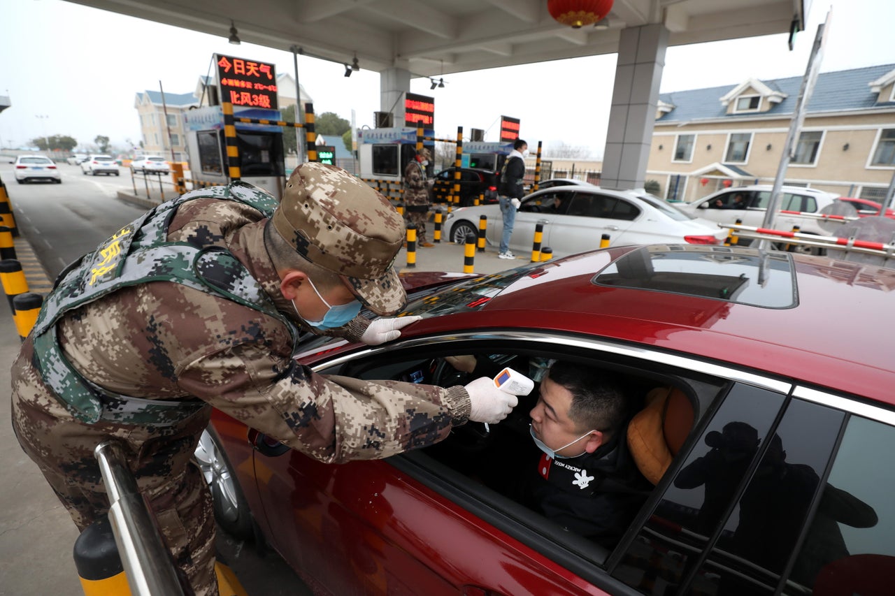 A driver has his temperature checked as he travels into Wuhan, with traffic police still allowing people to drive into the city 