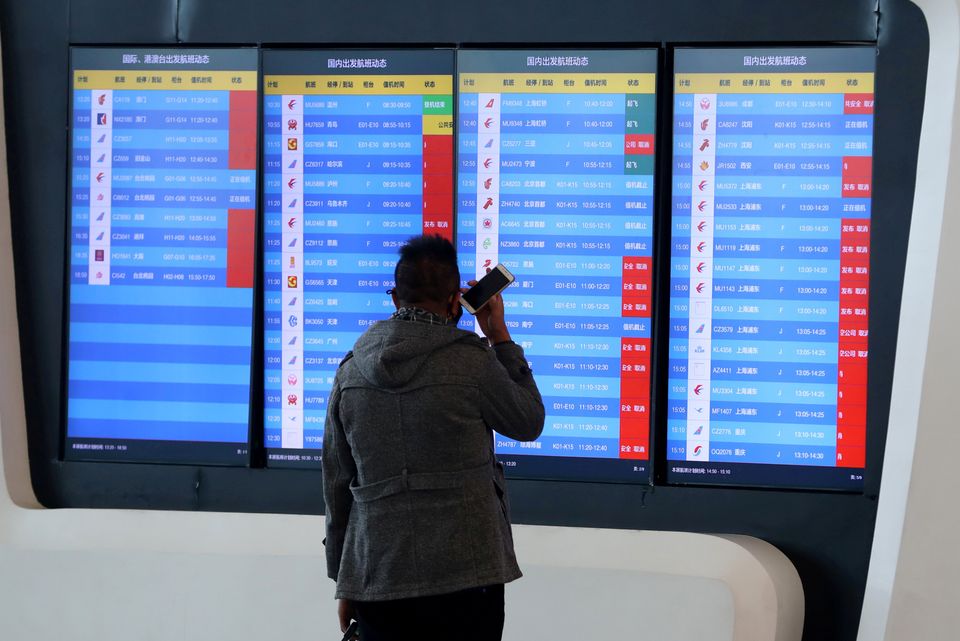 A man stands in front of a screen showing that multiple departure flights have been cancelled after the city was locked down 