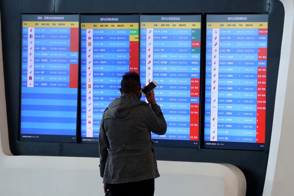 A man stands in front of a screen showing that multiple departure flights have been cancelled after the city was locked down 