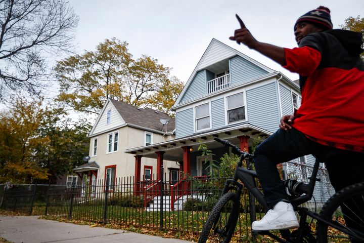A pedestrian stops outside the former home, in blue, of Tyesha Edwards, an 11-year-old girl pierced in the heart by a stray bullet in 2002 while doing homework at her family's dining room table, Wednesday, Oct. 23, 2019, in Minneapolis. (AP Photo/John Minchillo)
