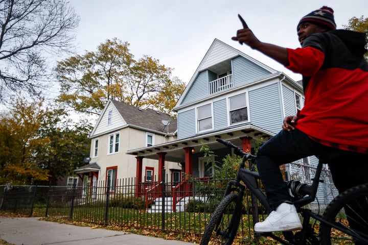 A pedestrian stops outside the former home, in blue, of Tyesha Edwards, an 11-year-old girl pierced in the heart by a stray bullet in 2002 while doing homework at her family's dining room table, Wednesday, Oct. 23, 2019, in Minneapolis. (AP Photo/John Minchillo)