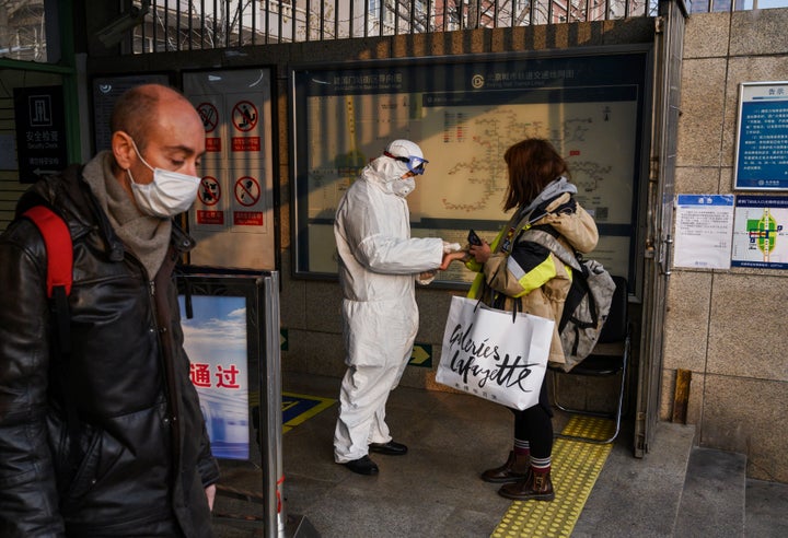 A Chinese worker is dressed in a protective suit as he takes the temperature of a woman at a subway station during the Chinese New Year and Spring Festival holiday on January 28, 2020 in Beijing, China. 