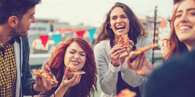 Happy group of people eating pizza outdoors