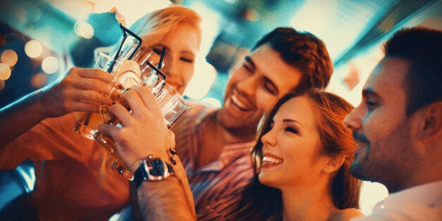 Group of young adult enjoying their night out in a club.Toasting with drinks,laughing and having casual conversation. Two couples on a double date.