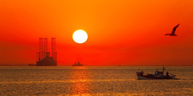 A traditional fishing boat and an offshore drilling rig during a colorful sunrise.