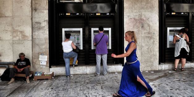 People withdraw money from ATM machines next to a beggar in Thessaloniki on 29 June, 2016. For a year the Greeks had to get used to not being able to withdraw more than 420 euros per week from the bank, a measure decided by credit control in full emergency which contributed to the stagnation of the economy. / AFP / SAKIS MITROLIDIS (Photo credit should read SAKIS MITROLIDIS/AFP/Getty Images)