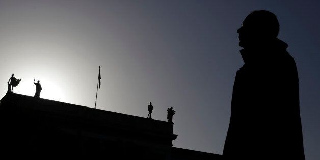 A pedestrian walks past statues, which stand at the top of the National Archaeological Museum of Greece in central Athens, on Thursday, Feb. 26, 2015. Greece's prime minister Alexis Tsipras held a marathon meeting with his party's lawmakers Wednesday, briefing them on pledges made to European creditors to win a four-month extension of the country's bailout amid simmering party discontent over what some see as a capitulation. The meeting, which was held behind closed doors, lasted more than 11 hours. (AP Photo/Petros Giannakouris)
