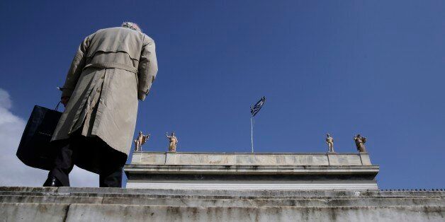 A pedestrian walks past statues, which stand at the top of the National Archaeological Museum of Greece as a Greek flag flies in central Athens, on Monday, March 16, 2015. Greece has slipped back into deficit so far this year, according to figures from the Bank of Greece. But the country's left-wing Prime Minister Alexis Tsipras ruled out any difficulties in making payments for public sector workers' salaries or state-backed pensions. (AP Photo/Petros Giannakouris)