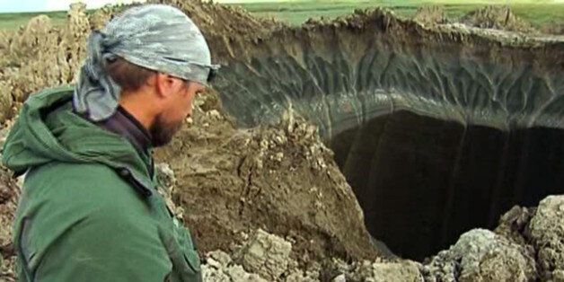 In this frame grab made Wednesday, July 16, 2014, Andrei Plekhanov, a senior researcher at the Scientific Research Center of the Arctic, stands at a crater, discovered recently in the Yamal Peninsula, in Yamalo-Nenets Autonomous Okrug, Russia. Russian scientists said Thursday july 17, 2014 that they believe a 60-meter wide crater, discovered recently in far northern Siberia, could be the result of changing temperatures in the region. Andrei Plekhanov said 80 percent of the crater appeared to be