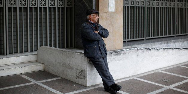 A protester sits in front of the shuttered entrance of Greece's Central Bank during a 24-hour nationwide general strike, in Athens, Thursday Nov. 27, 2014. A nationwide general strike to protest continued austerity measures has shut down services across Greece, grounding flights, leaving ferries tied up in ports, shutting down schools and leaving state hospitals functioning with emergency staff. Greece has been dependent on billions of euros from international bailouts from the eurozone and International Monetary Fund since 2010. (AP Photo/Kostas Tsironis)