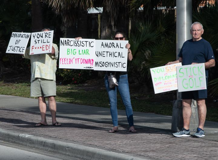 Protesters hold signs as President Donald Trump's motorcade makes its way to the Trump International Golf Club in West Palm Beach, Florida, on April 20, 2019. 