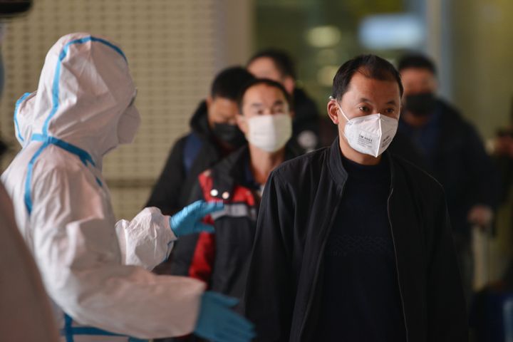 Masked travellers pass by a screening worker at a railway station in Nanjing in east China's Jiangsu province